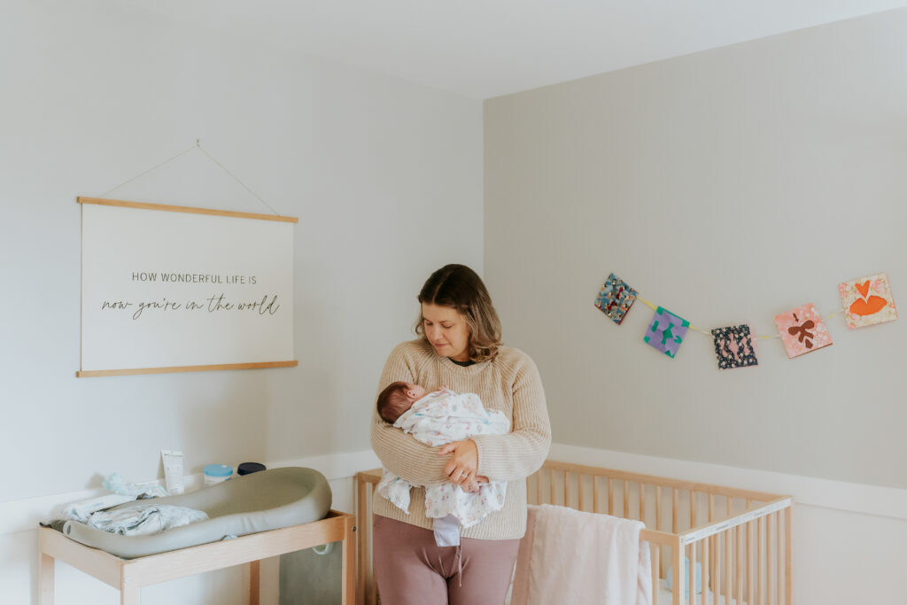mom holding baby next to a crib